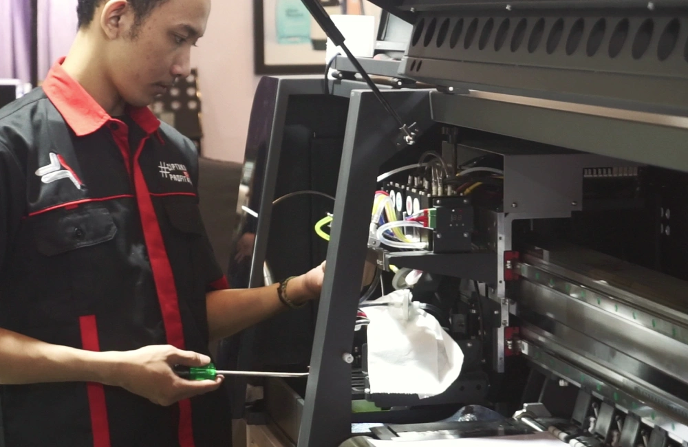 Seorang teknisi sedang membersihkan area printer dari kotoran.