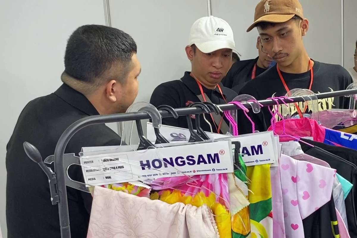 Visitors discussing apparel printing samples at IAPE 2025 exhibition booth.