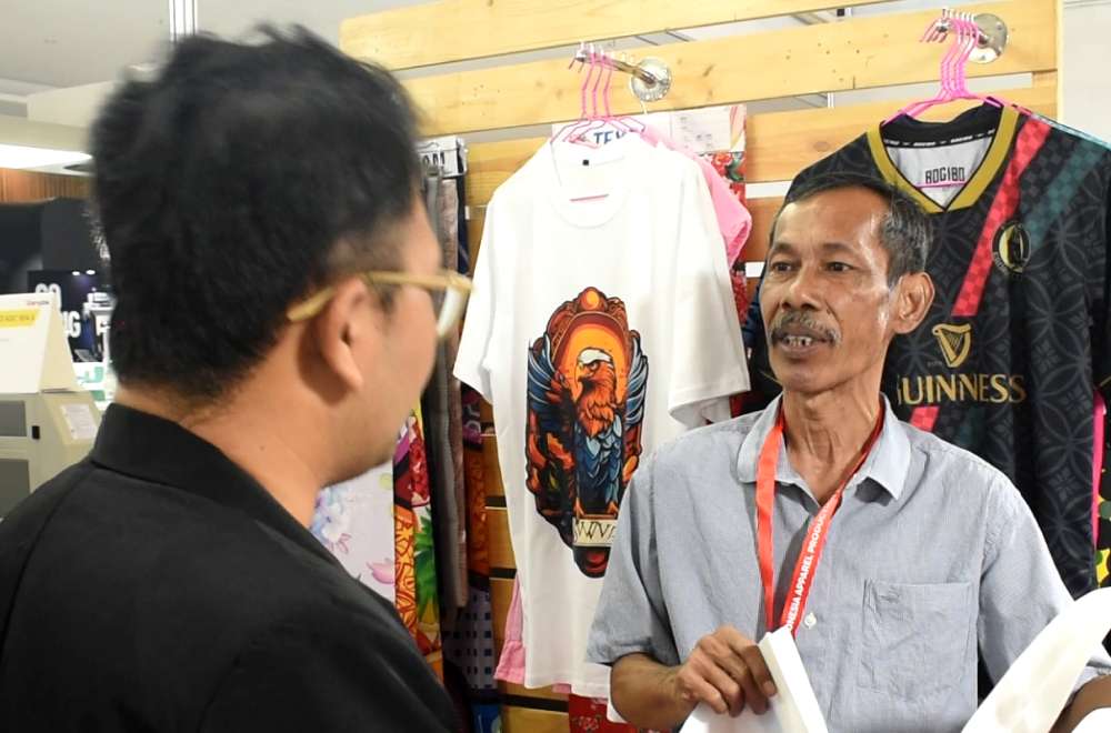 Visitor discussing apparel printing products and promotions at Laysander booth during IAPE 2025.