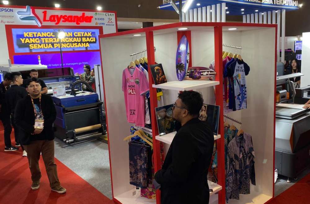 Booth Laysander di pameran All Print 2025 menampilkan berbagai hasil cetak kreatif seperti kaus, papan, dan produk promosi.