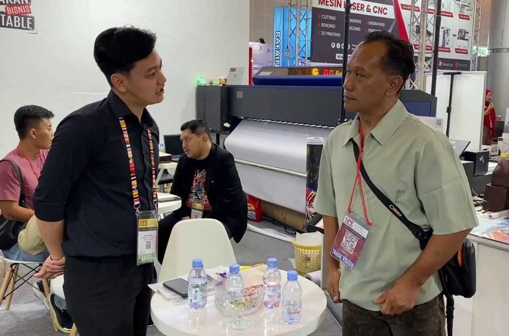 Perwakilan exhibitor berdiskusi dengan pengunjung di booth Surabaya Printing Expo 2026 mengenai teknologi mesin cetak dan peluang pengembangan bisnis.