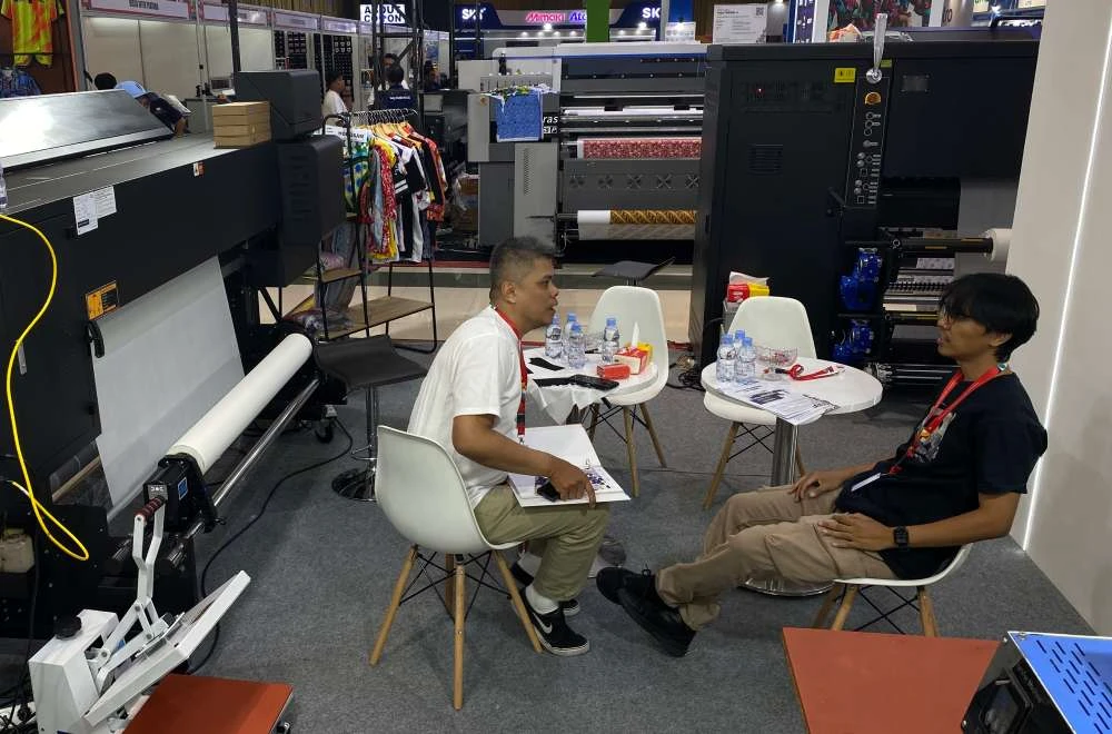 Pengunjung berkonsultasi dengan tim ahli di tengah jajaran mesin printing pada pameran IAPE Bandung 2026.